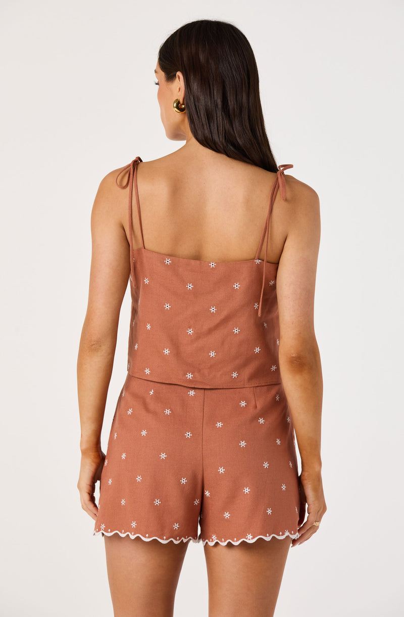 Woman in matching rust-colored top and shorts with white floral embroidery and scalloped hem.