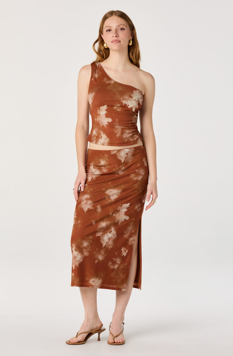 Woman wearing a brown tie-dye one-shoulder crop top and matching high-waisted skirt with a slit.