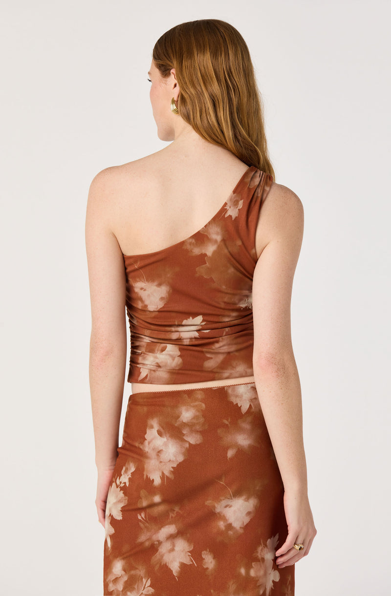 Woman wearing a rust-colored, tie-dye one-shoulder crop top and matching skirt.