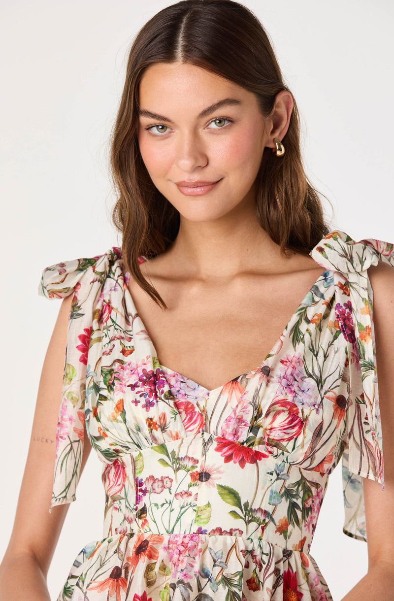 Young woman in a sleeveless, floral dress with bow-tied shoulder straps.