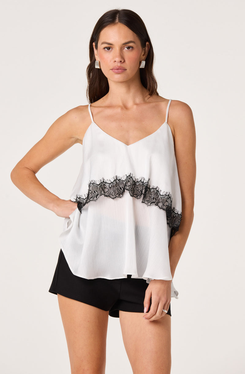 Woman wearing a white sleeveless top with black lace trim and black shorts.