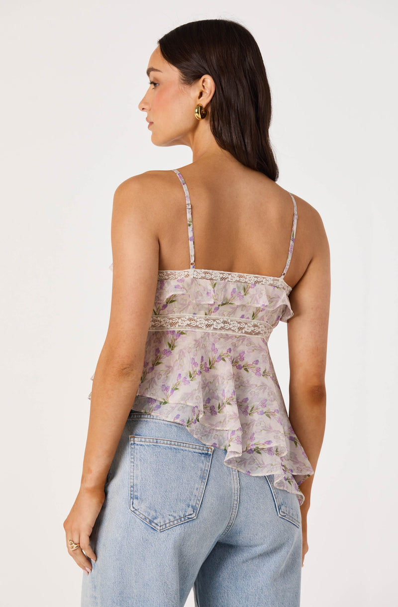 Woman wearing a lilac floral spaghetti strap top with lace details and a ruffled hem.