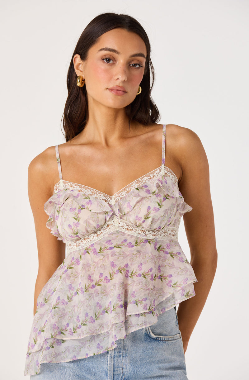 Woman in a pastel floral camisole with ruffles and lace details, paired with jeans.