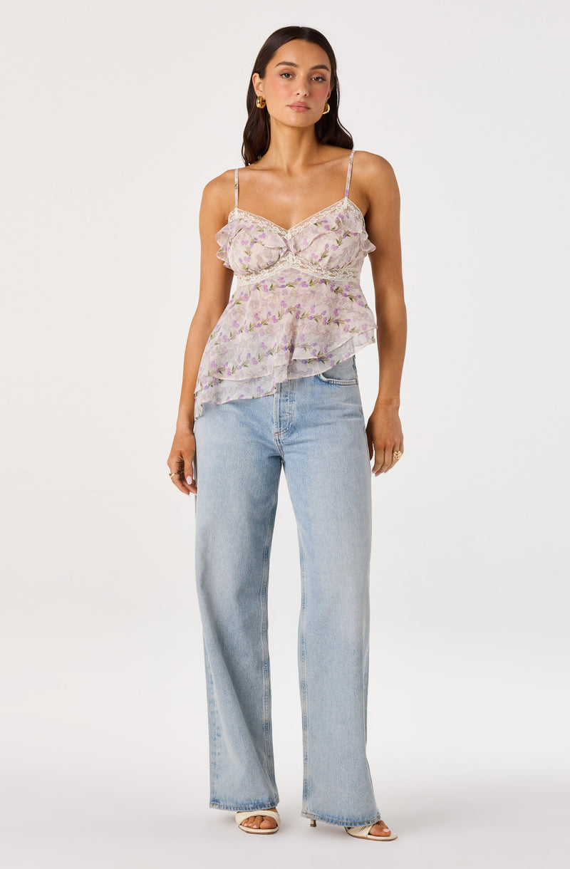 Woman wearing a light purple floral ruffled top with spaghetti straps and wide-leg light blue jeans.