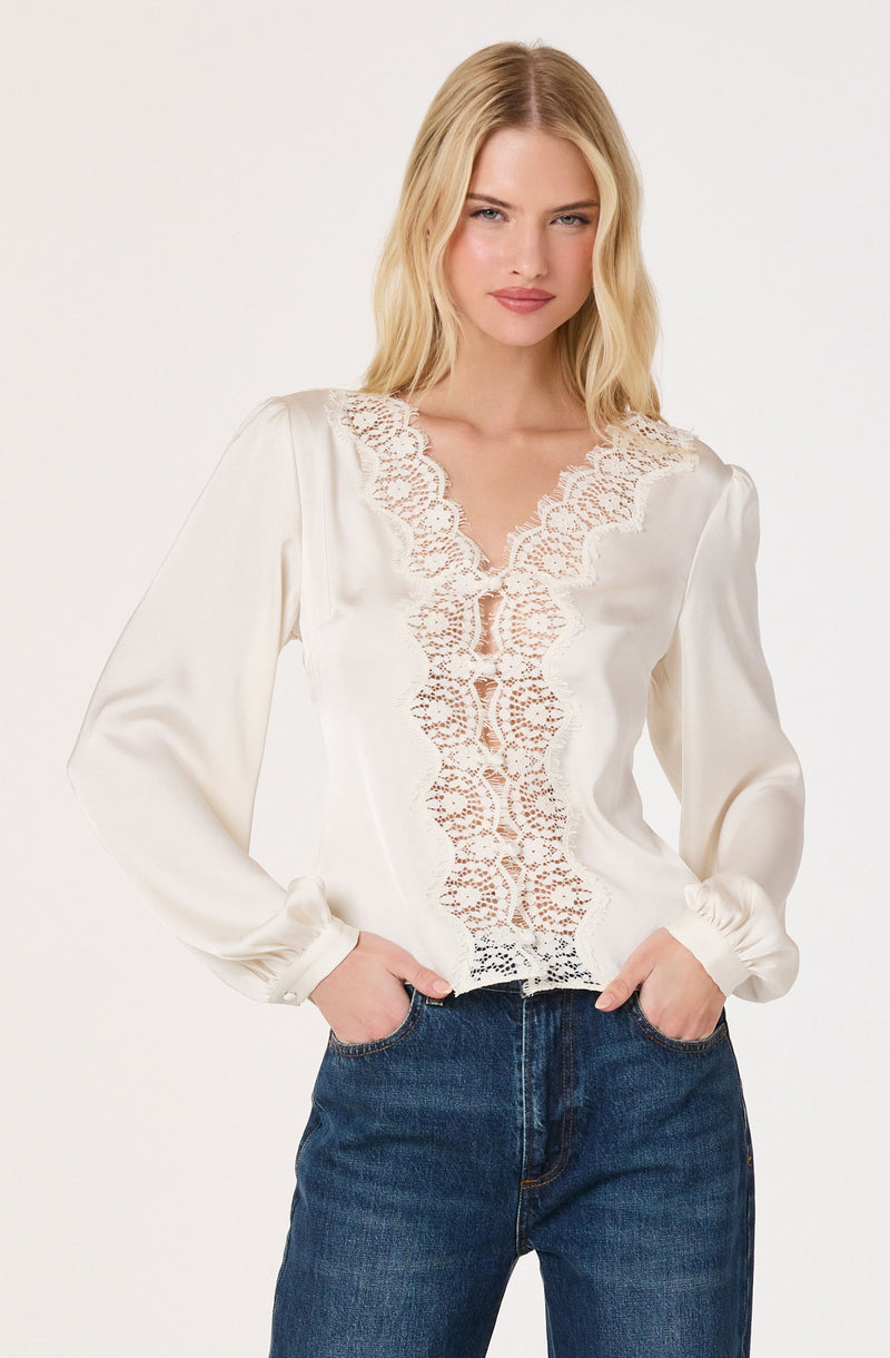 Woman wearing a white satin blouse with lace detailing and long puffed sleeves.