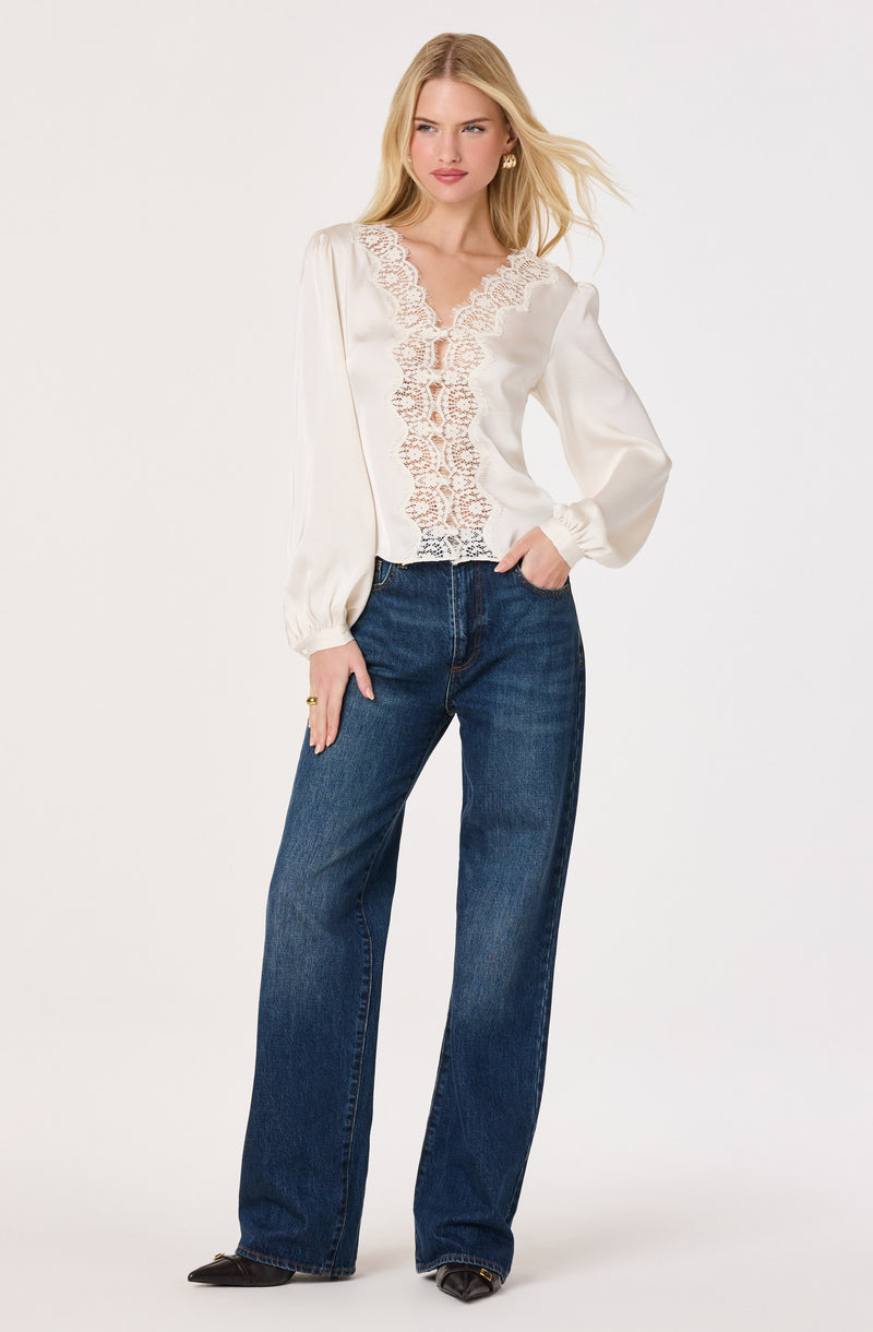 Woman wearing a cream satin blouse with lace detailing and puff sleeves, paired with high-waisted blue jeans.