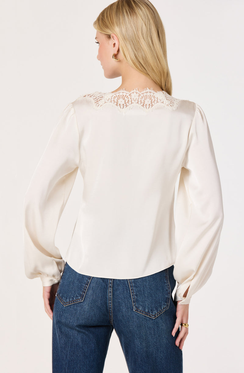 Woman in white satin blouse with lace detail on shoulders and puffed long sleeves.