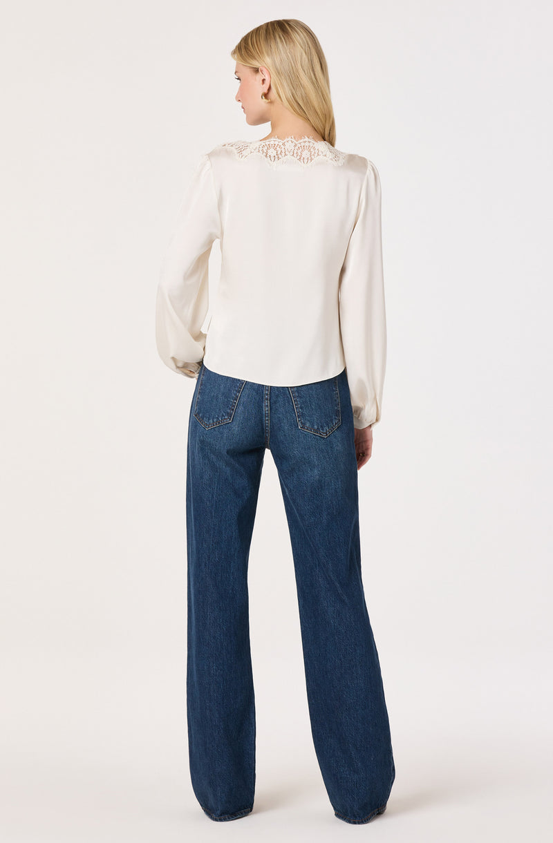 Woman wearing a white long-sleeve blouse with lace details on the back, paired with high-waisted blue jeans.
