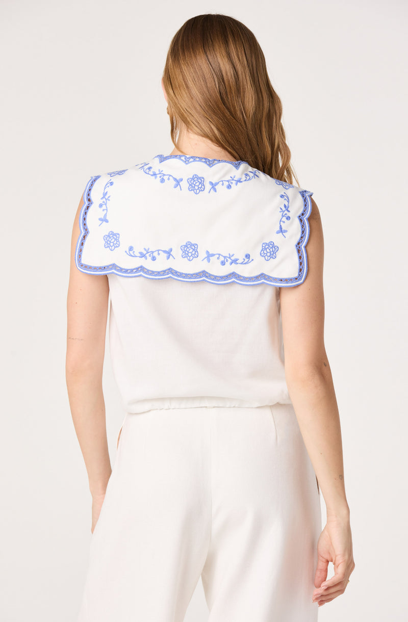 Woman wearing a white top with a large, embroidered white collar with blue floral designs.