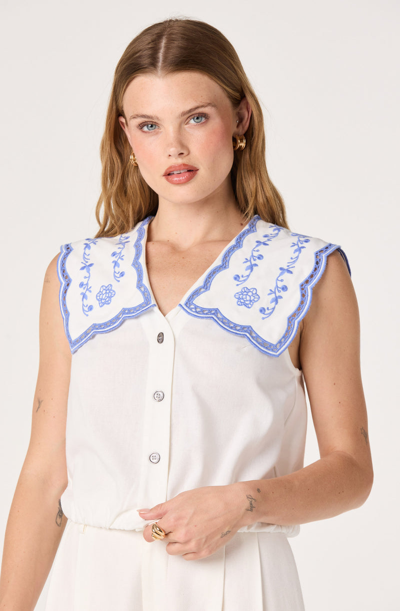 White sleeveless top with a large, scalloped blue embroidered collar.