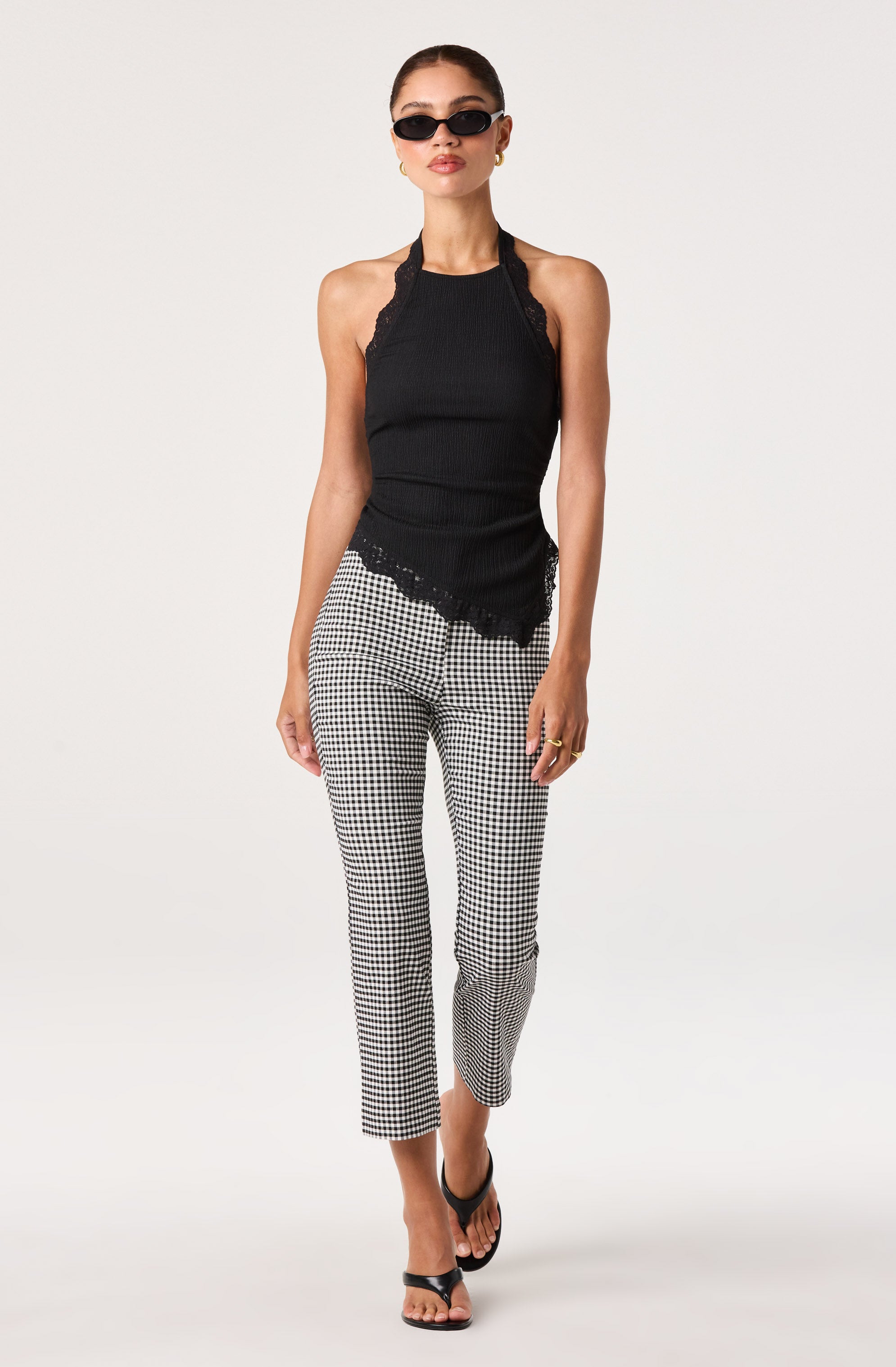 Woman wearing a black sleeveless top with lace details and checkered black-and-white pants.