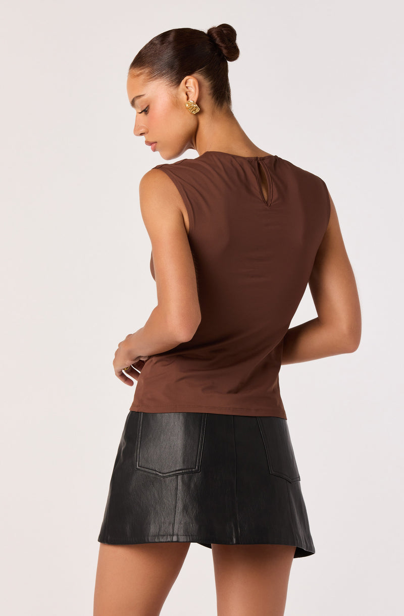 Woman in sleeveless brown top and black leather skirt, facing away with hair in a bun.