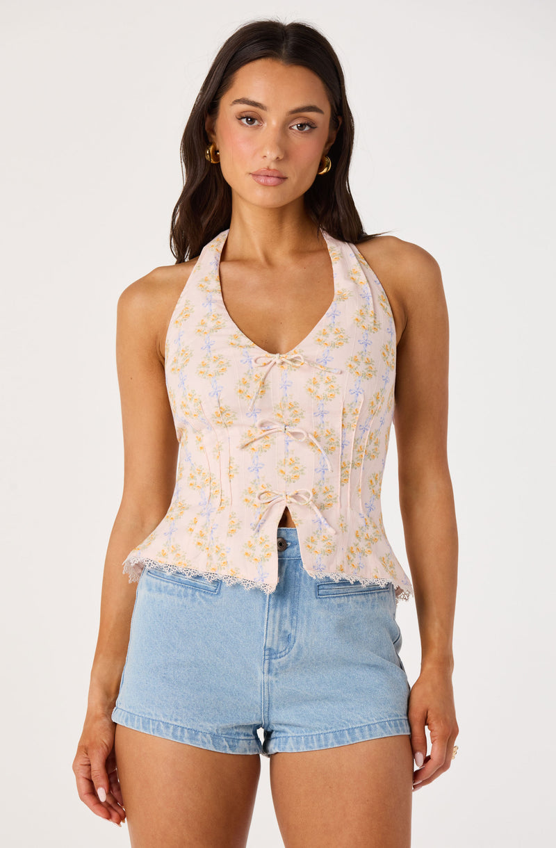 Woman in sleeveless, floral, lace-trimmed top with a bow, paired with high-waisted light blue denim shorts.