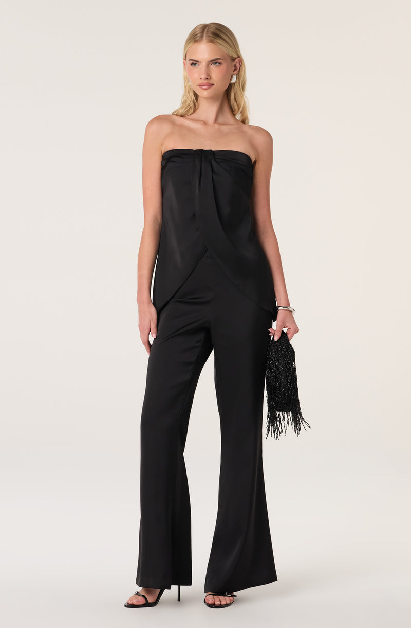 Woman in a strapless black satin jumpsuit, holding a black beaded clutch.