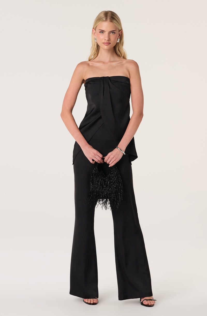 Woman in a black strapless satin top and matching wide-leg pants, holding a black beaded clutch.