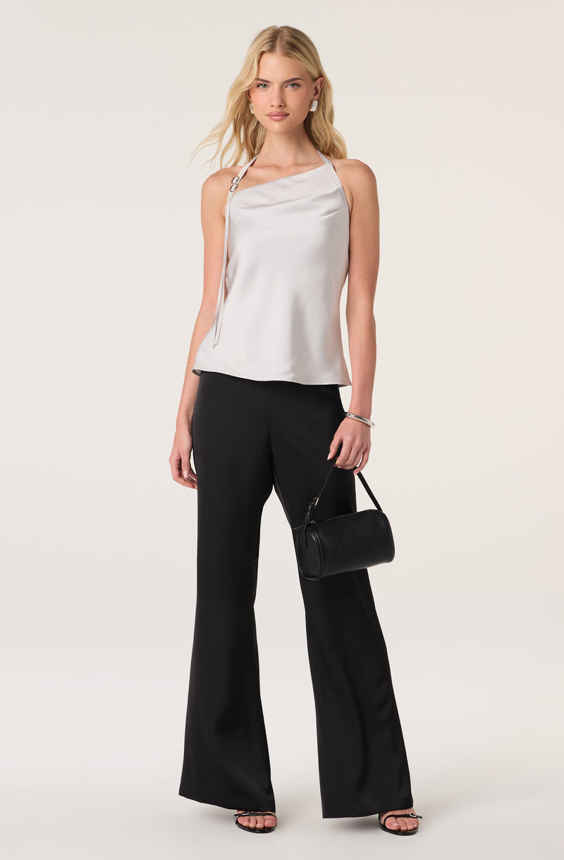 Woman in a white satin sleeveless top with thin straps and black wide-leg pants, holding a black handbag.