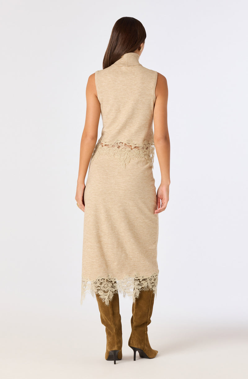 Beige sleeveless dress with lace details at the waist and hem, paired with brown high-heeled boots.