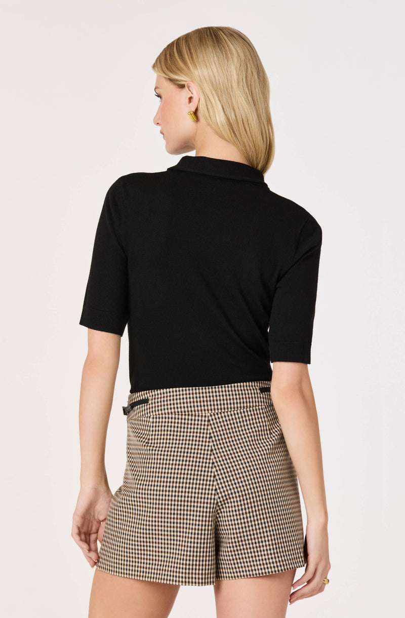 Woman wearing a black short-sleeve top and beige checkered shorts.