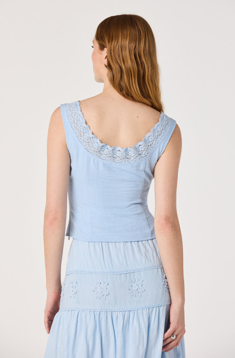 Back view of a woman in a light blue sleeveless top with lace trim, paired with a matching embroidered skirt.