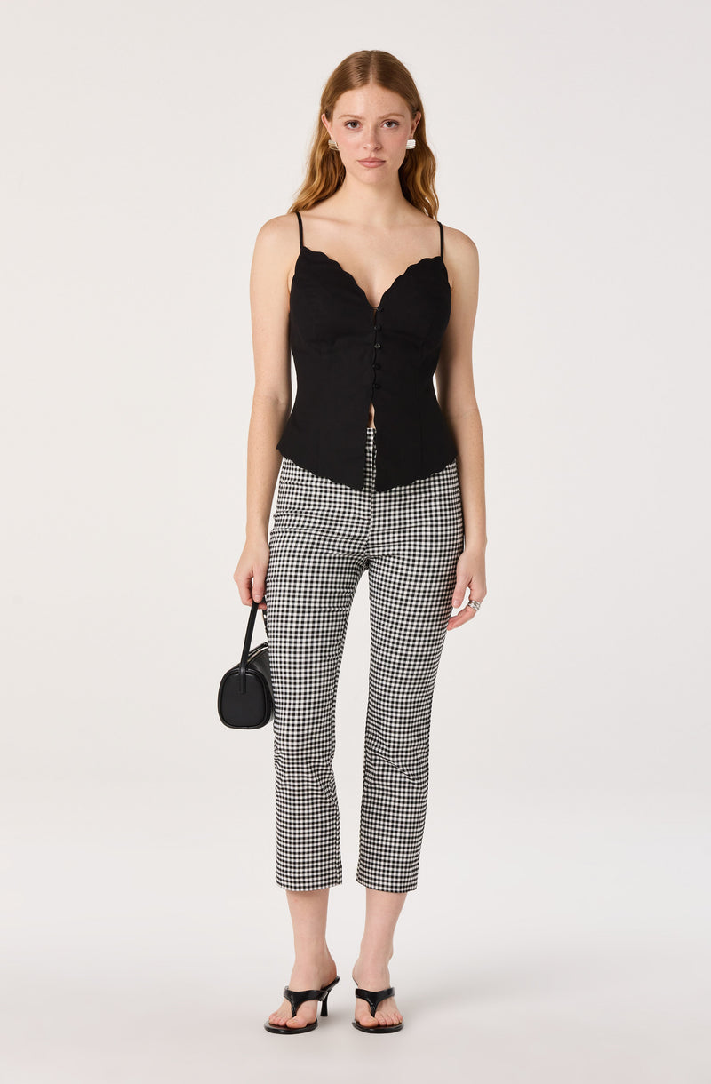 Woman in black sleeveless top and black-and-white checkered pants, holding a black bag.