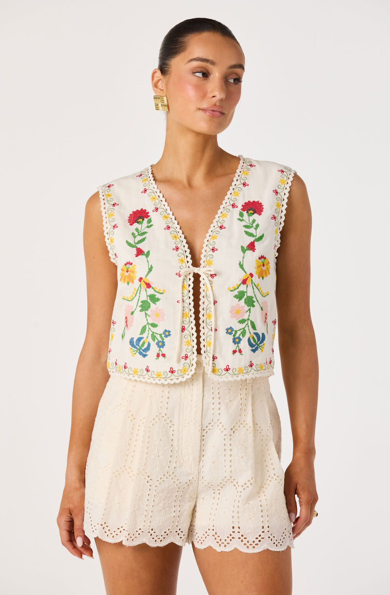 Cream embroidered sleeveless vest with colorful floral patterns and scalloped edges over matching eyelet shorts.