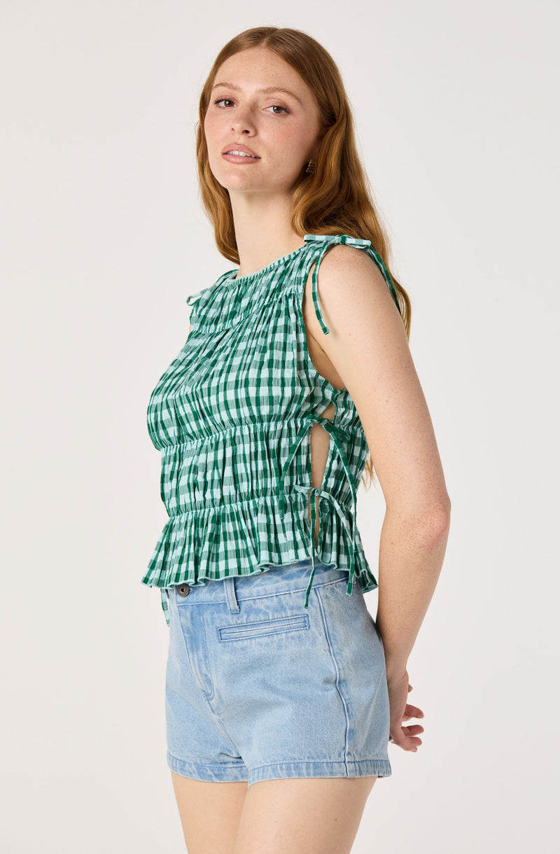 Woman in green and white checkered sleeveless top with side ties, paired with light blue denim shorts.