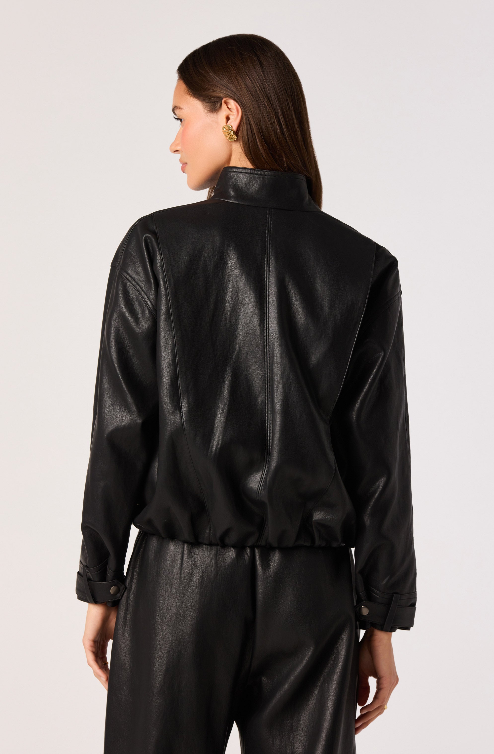 Woman wearing a black leather jacket with a high collar and matching black leather pants.