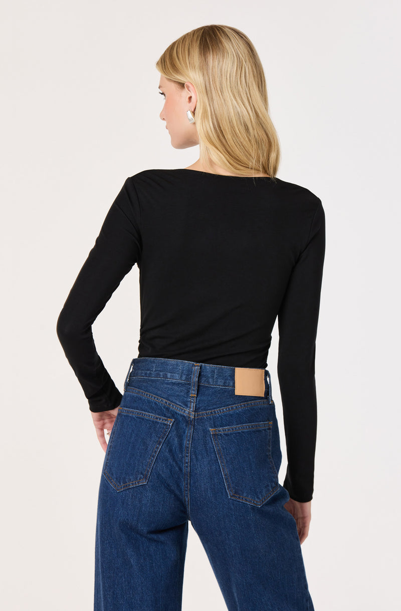 Woman wearing a black long sleeve top and high-waisted blue jeans with a beige label.