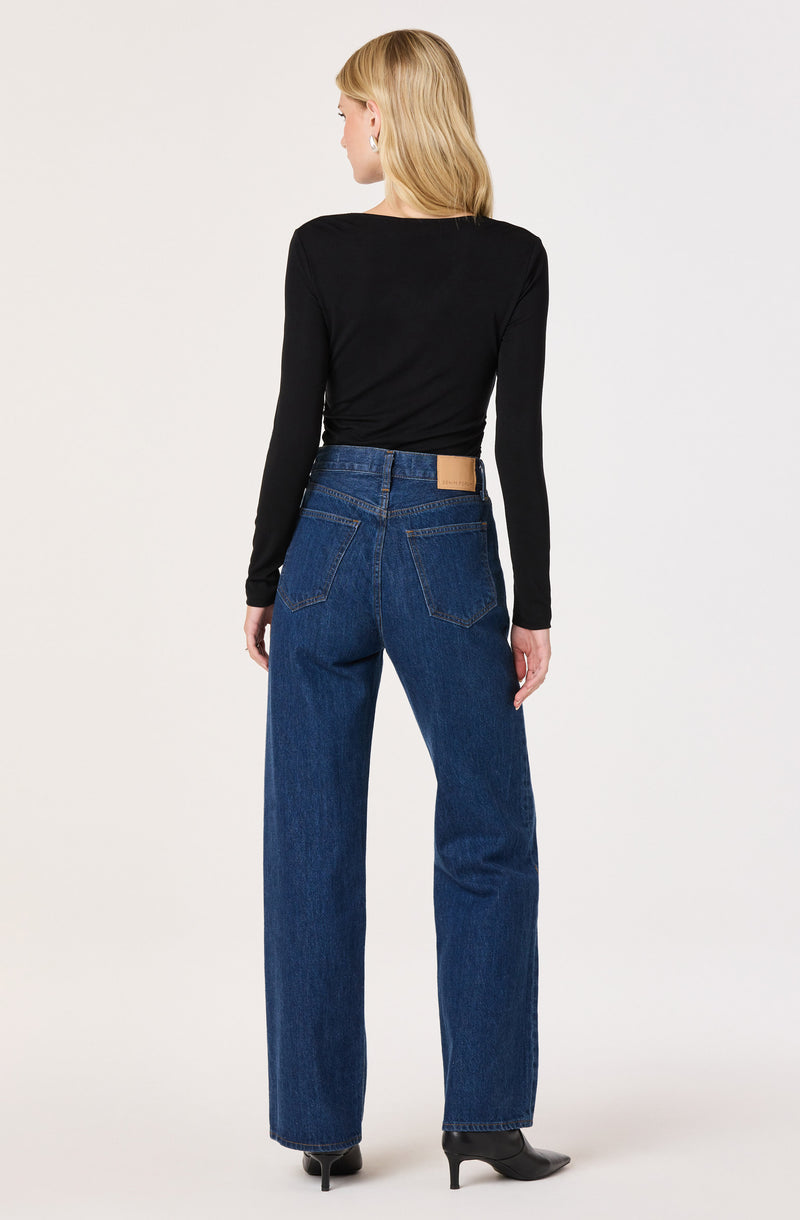 Woman wearing a black long-sleeve top, high-waisted blue jeans, and black boots.