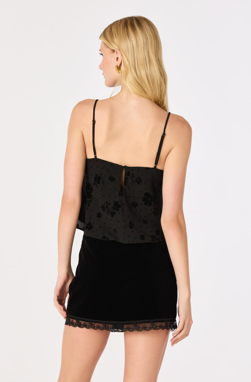 Woman in a black spaghetti strap top with floral pattern and a black lace hem skirt.