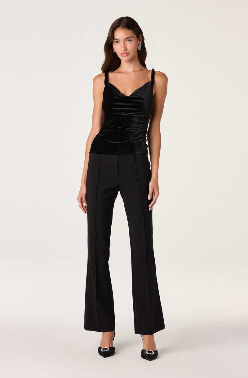 Woman in black velvet camisole top with thin straps and high-waisted black dress pants with flared legs.