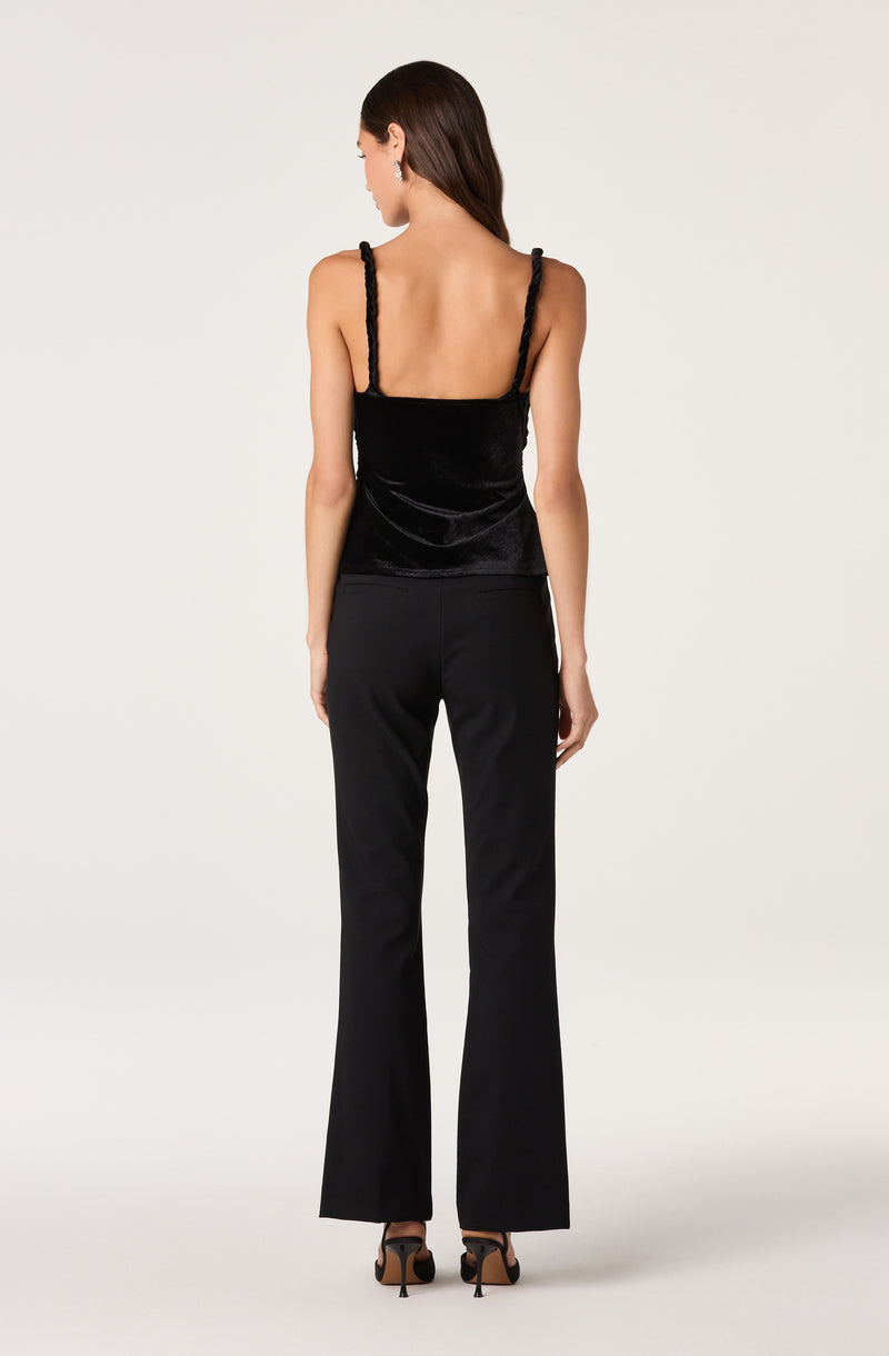 Woman wearing a black velvet sleeveless top with thin braided straps and black wide-leg pants.