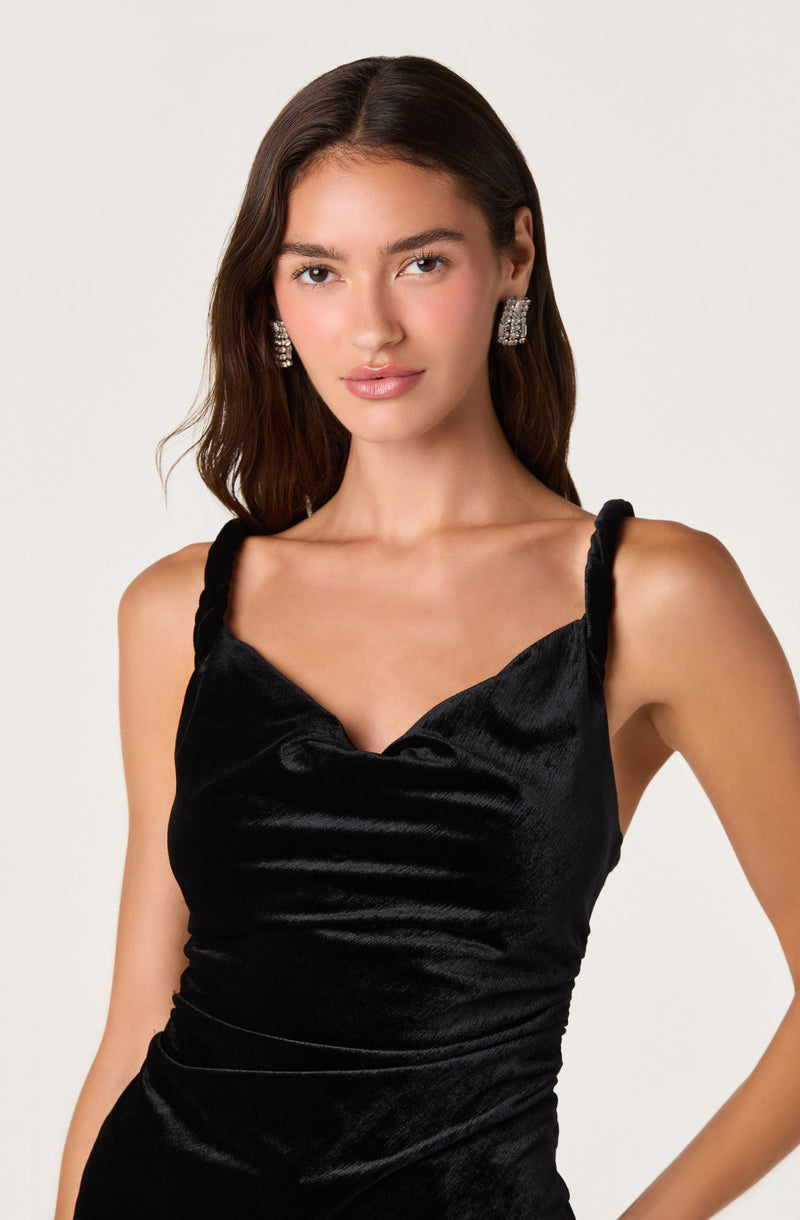 Woman in a black, satin, sleeveless dress with twisted straps and pleated fabric.