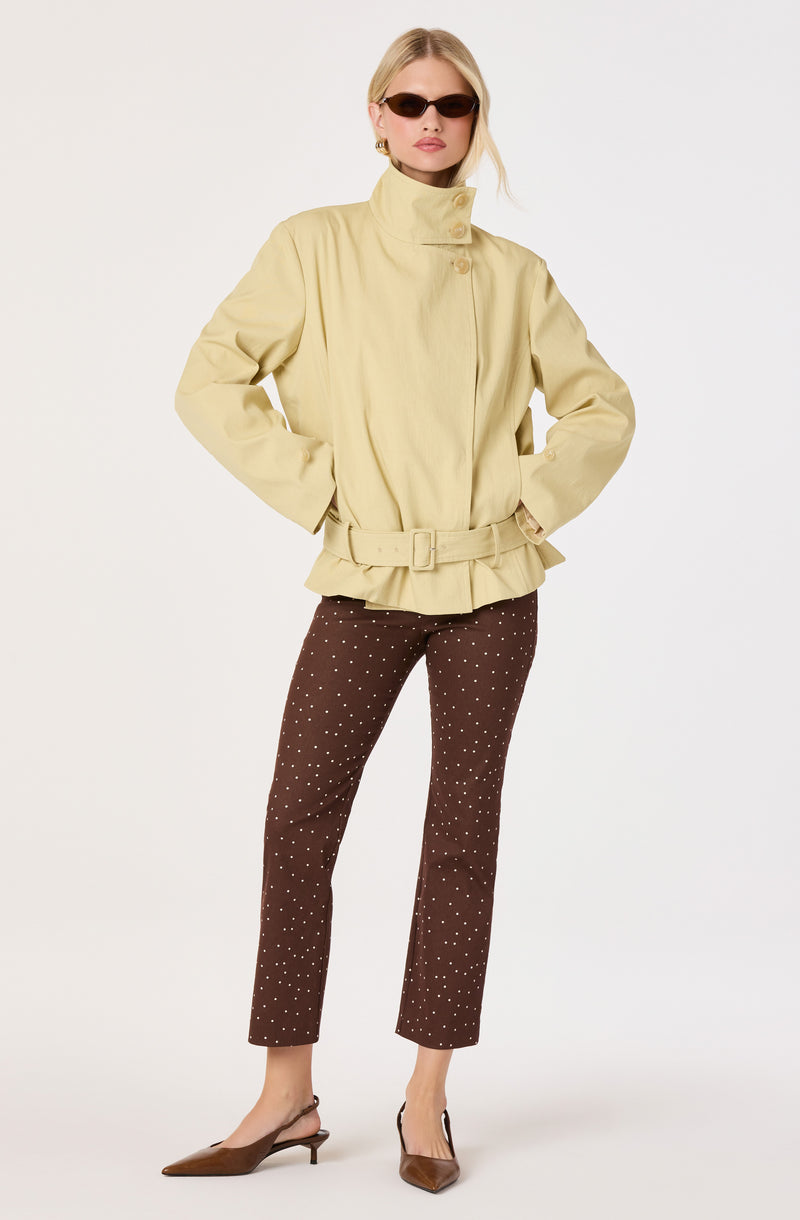 Woman in a beige belted jacket and brown polka dot pants with brown heels, wearing sunglasses.