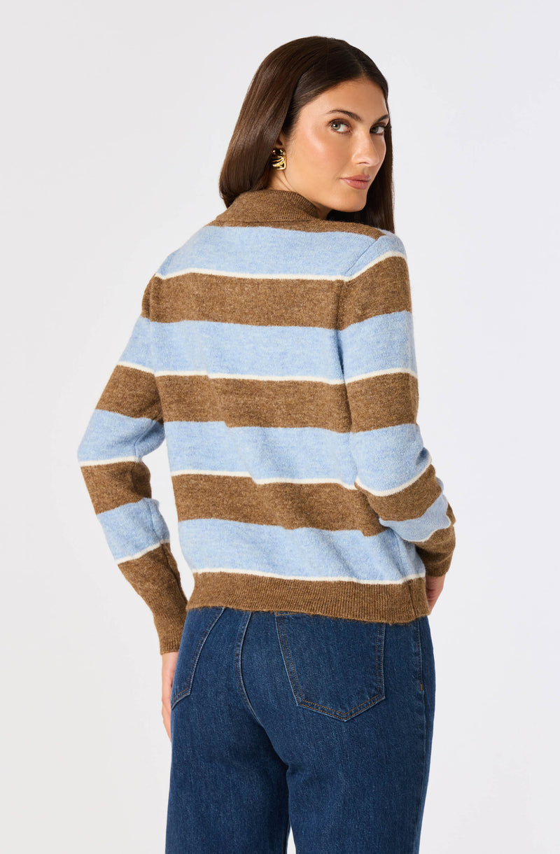 Woman wearing a brown and blue striped sweater and blue jeans.