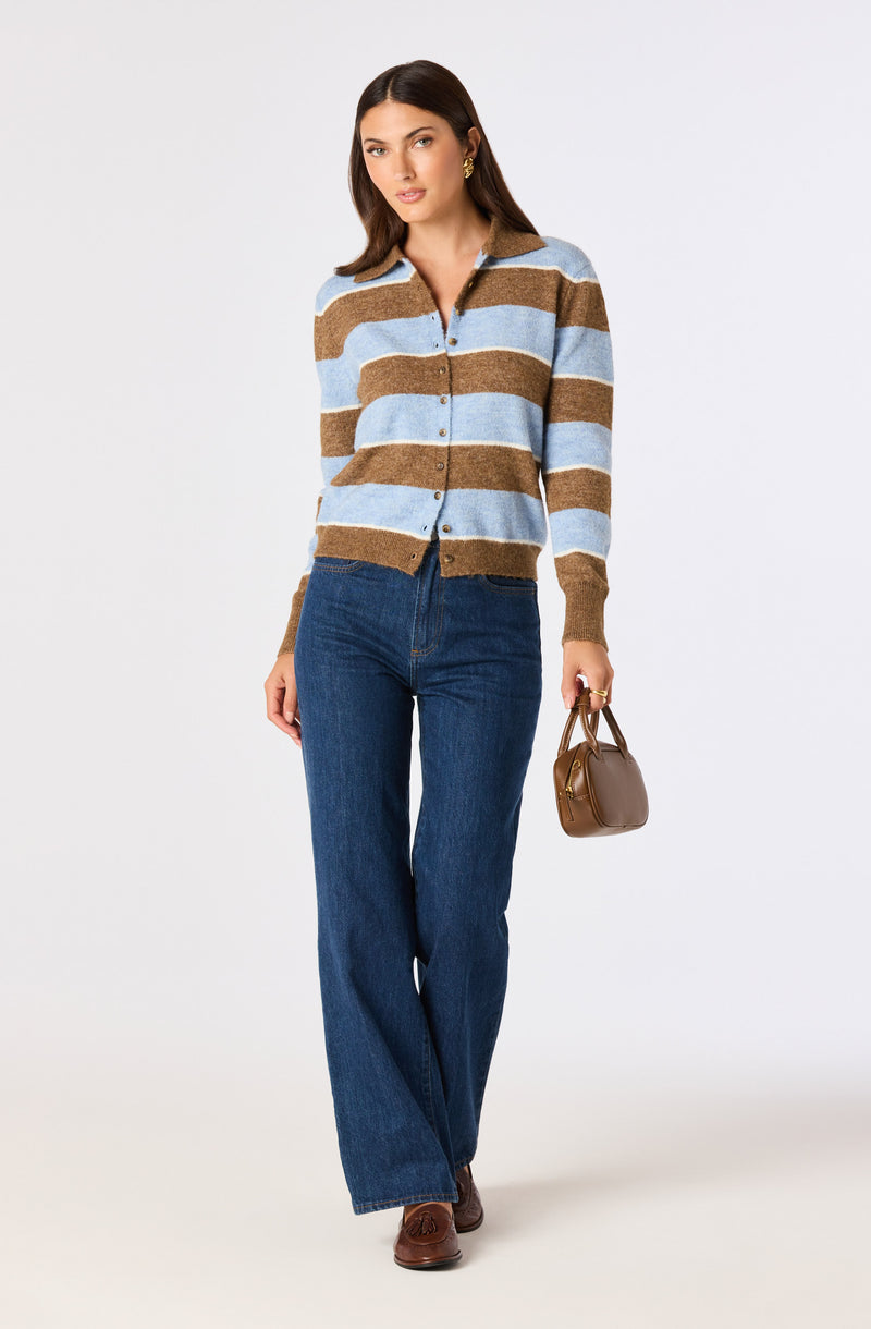 Woman wearing a striped brown and light blue cardigan, dark blue wide-leg jeans, brown shoes, and holding a small brown handbag.