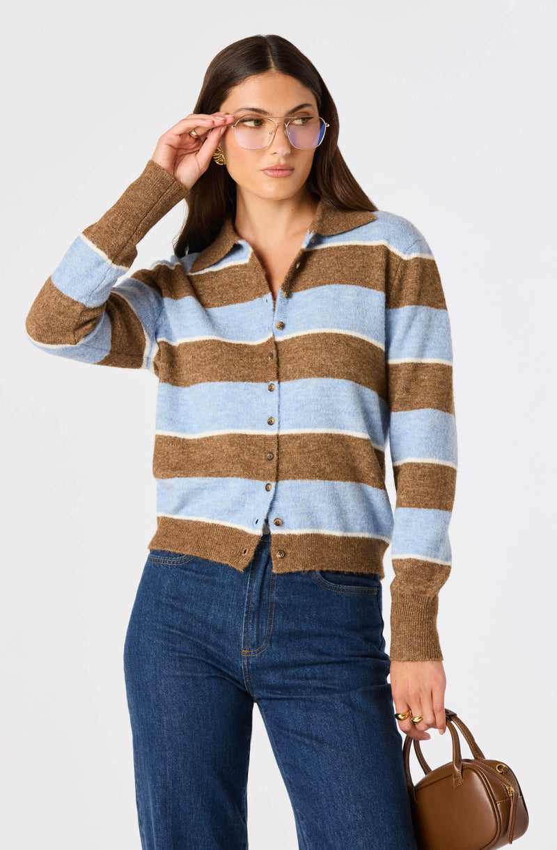Woman wearing a brown and light blue striped sweater with a collar and buttons, dark blue jeans, and gold glasses.