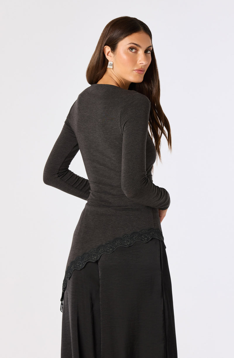 Woman wearing an all-black outfit with a fitted long-sleeve top with scalloped lace hem and a flowing skirt.