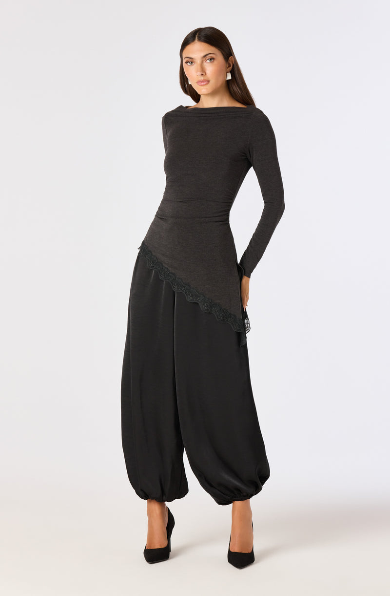 Woman in a fitted dark gray long-sleeve top with asymmetrical lace hem and wide black harem pants with gathered ankles.