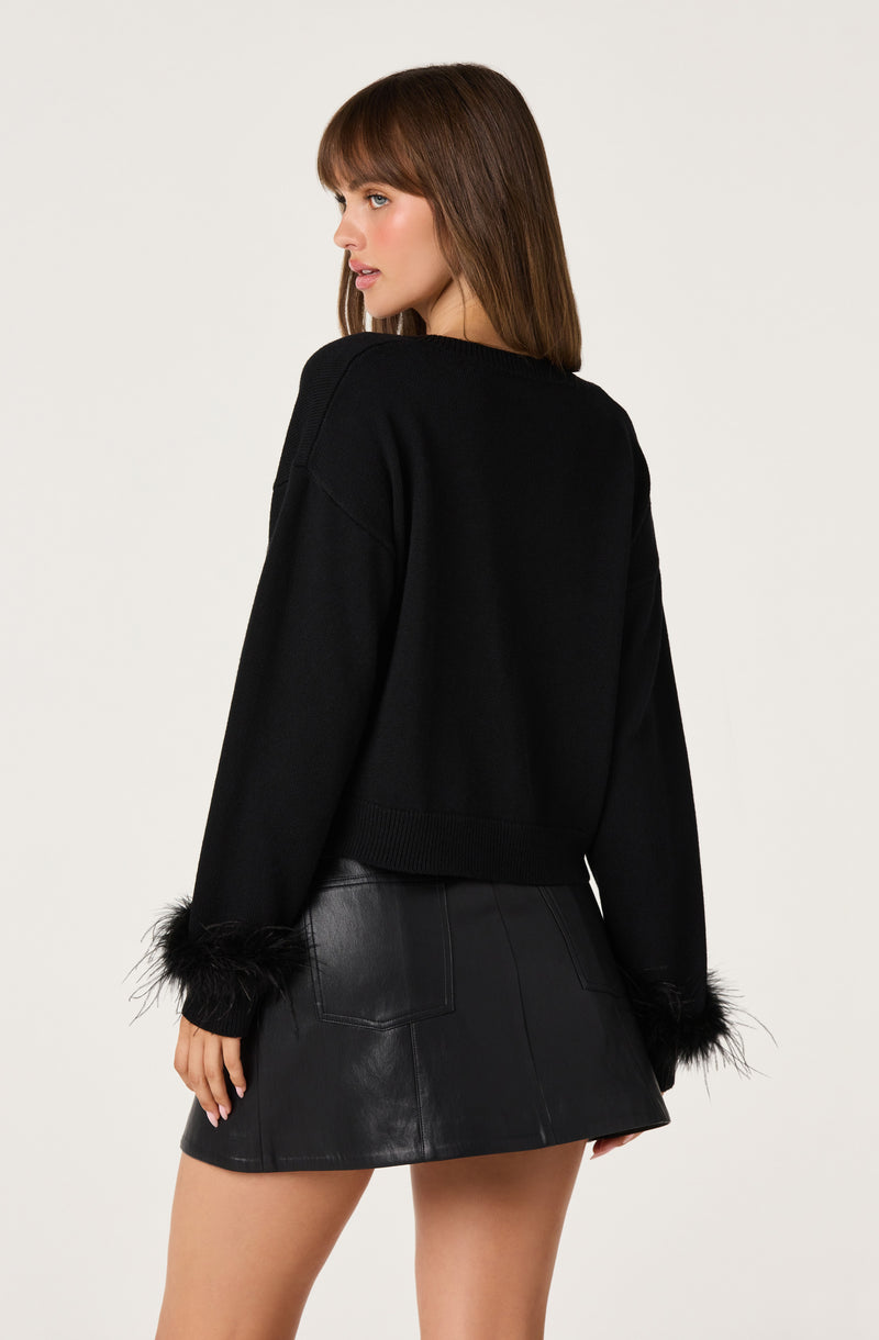 Woman wearing a black sweater with fur-trimmed cuffs and a black leather mini skirt.