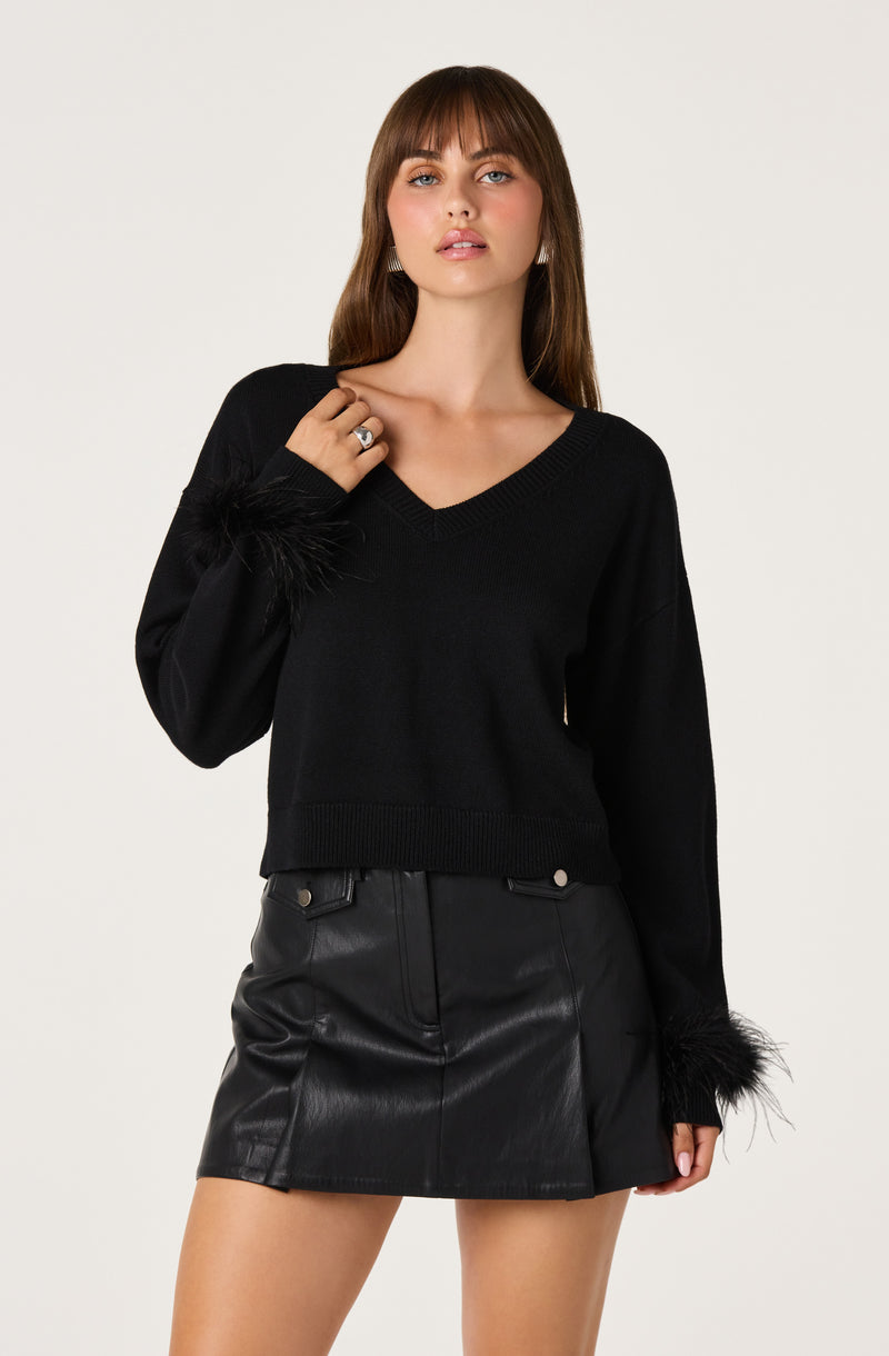 Woman in a black V-neck sweater with feathered cuffs and a black leather mini skirt.