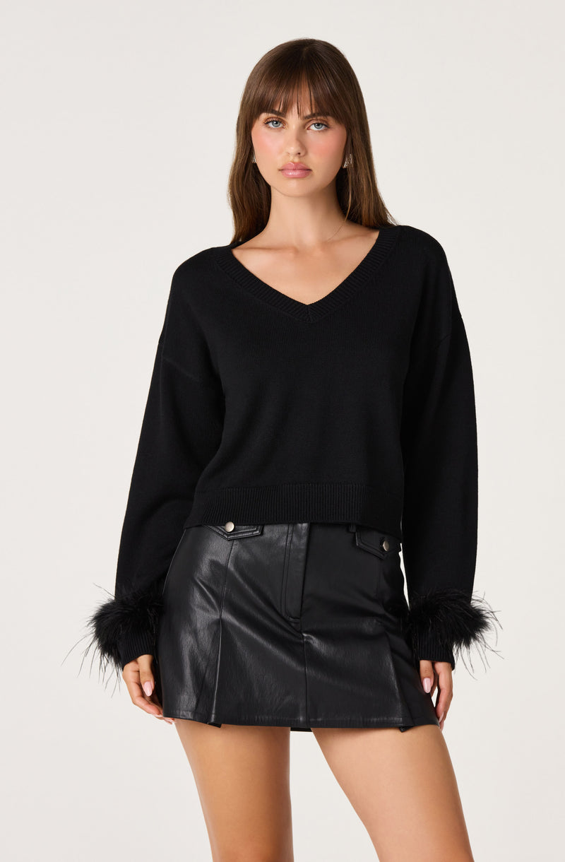 Woman wearing a black V-neck sweater with fur-trimmed cuffs and a black leather mini skirt.
