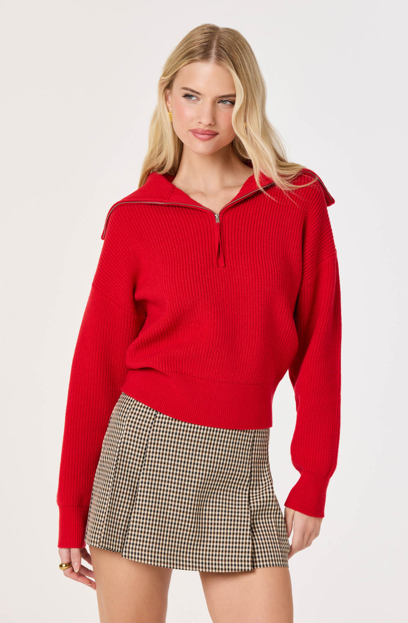 Woman wearing a red zip-up sweater and a beige checkered skirt.
