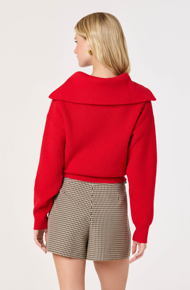 Woman wearing a red knit sweater with a wide collar and beige checkered shorts.