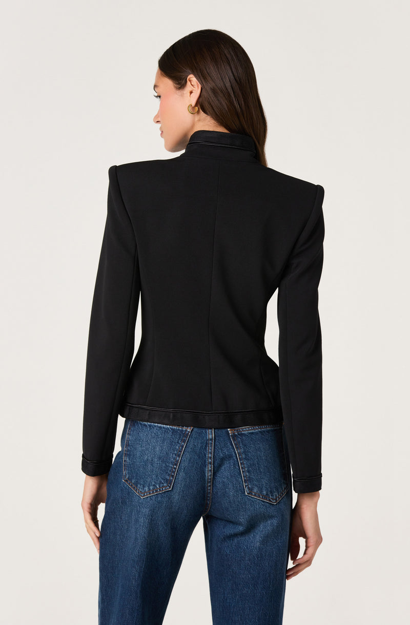 Woman in a tailored black blazer and blue jeans, facing away.