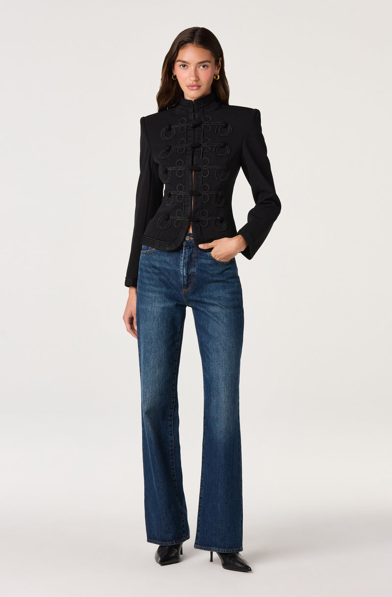 Woman in a black military-style jacket with loop decorative details and high neck, paired with blue wide-leg jeans.