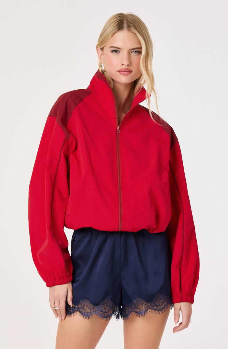 Woman wearing a red and dark red colorblock windbreaker jacket with a high collar.