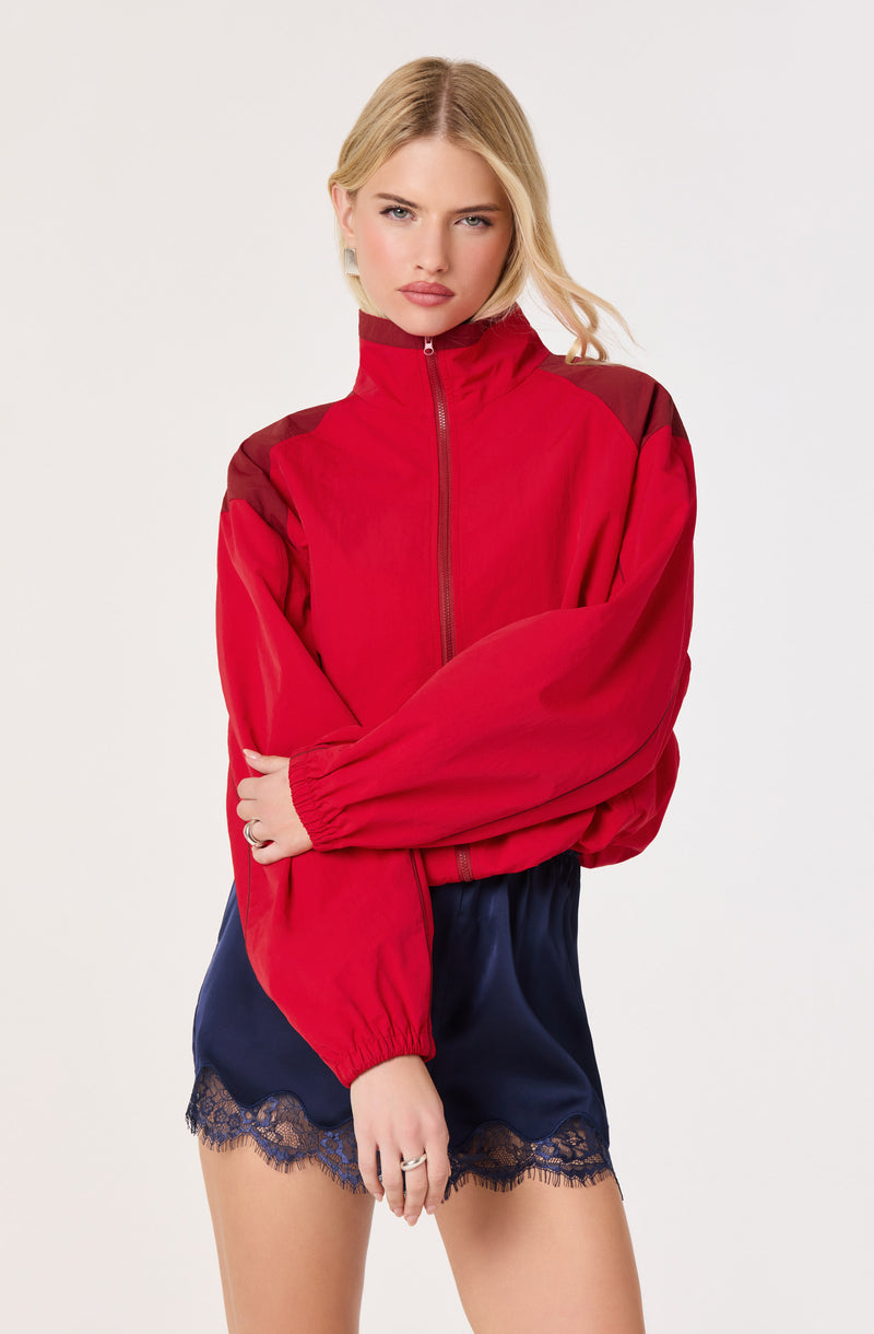 Woman wearing a red zip-up jacket with dark shoulder accents and navy lace-trimmed shorts.