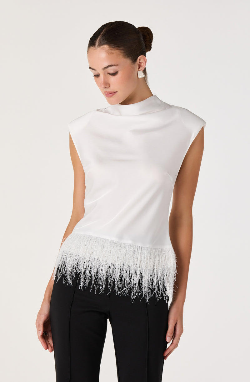 White sleeveless top with feathered hem and high neck, paired with black pants.