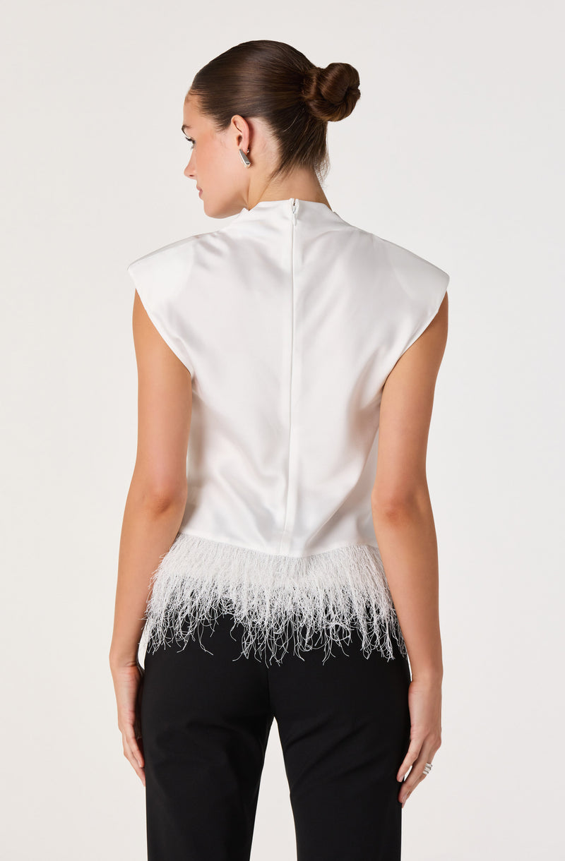 Woman wearing a white satin top with feathered hem and black pants.